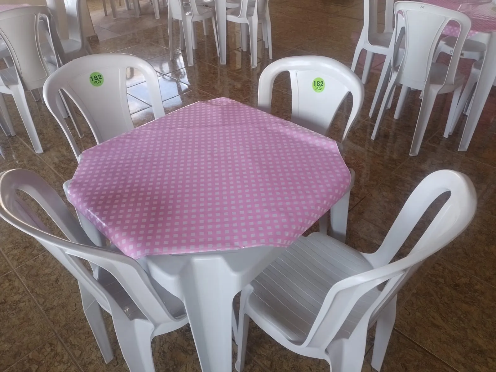Mesa com toalha rosa de poá e cadeiras brancas em salão de festas