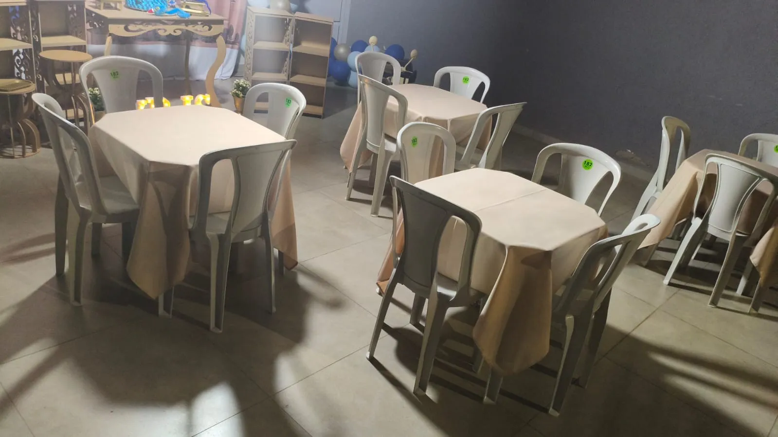 Salão com mesas cobertas por toalhas bege e cadeiras brancas